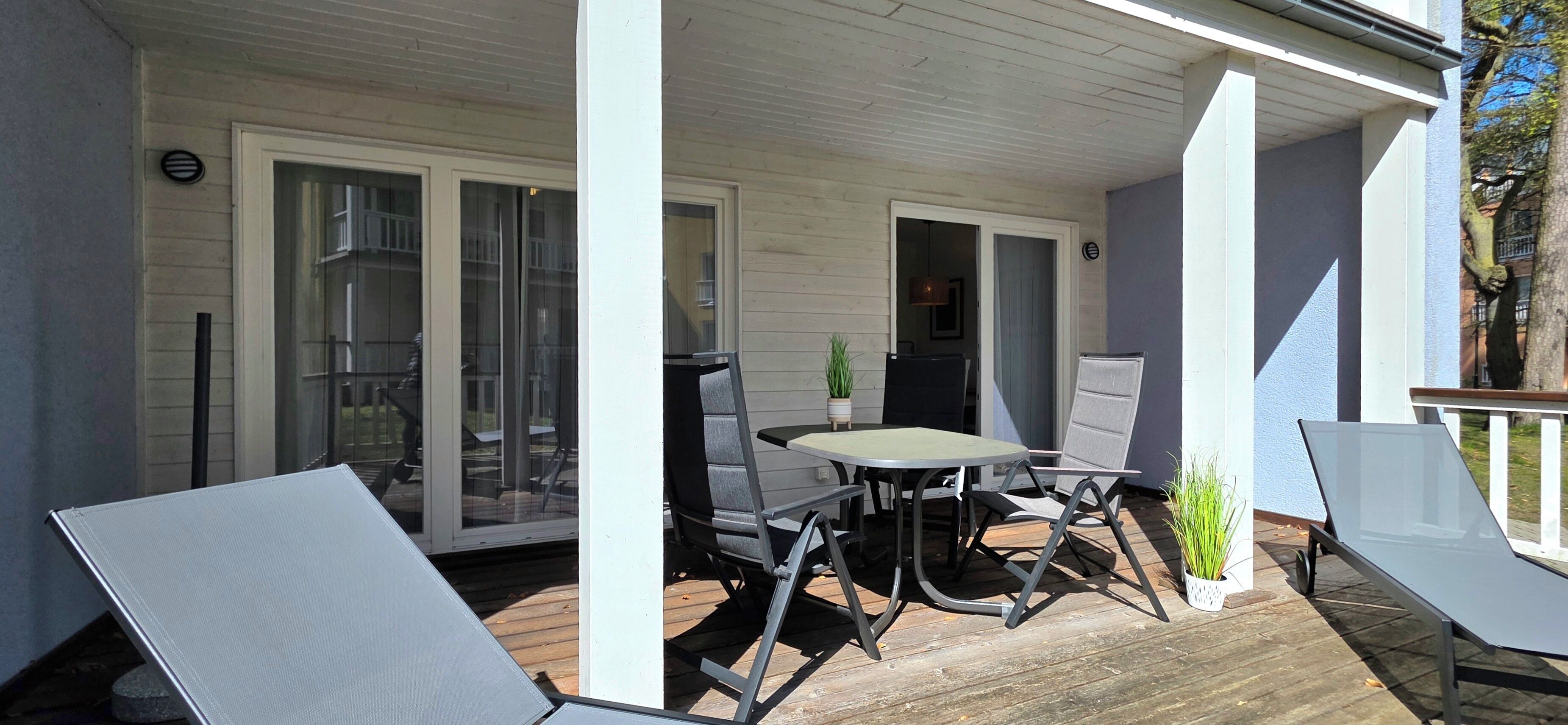 A covered patio with a table and chairs, a sliding glass door, and a potted plant.