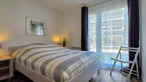 Une chambre à coucher avec un lit, une table de chevet, une lampe et une vue sur un balcon équipé d’une chaise.