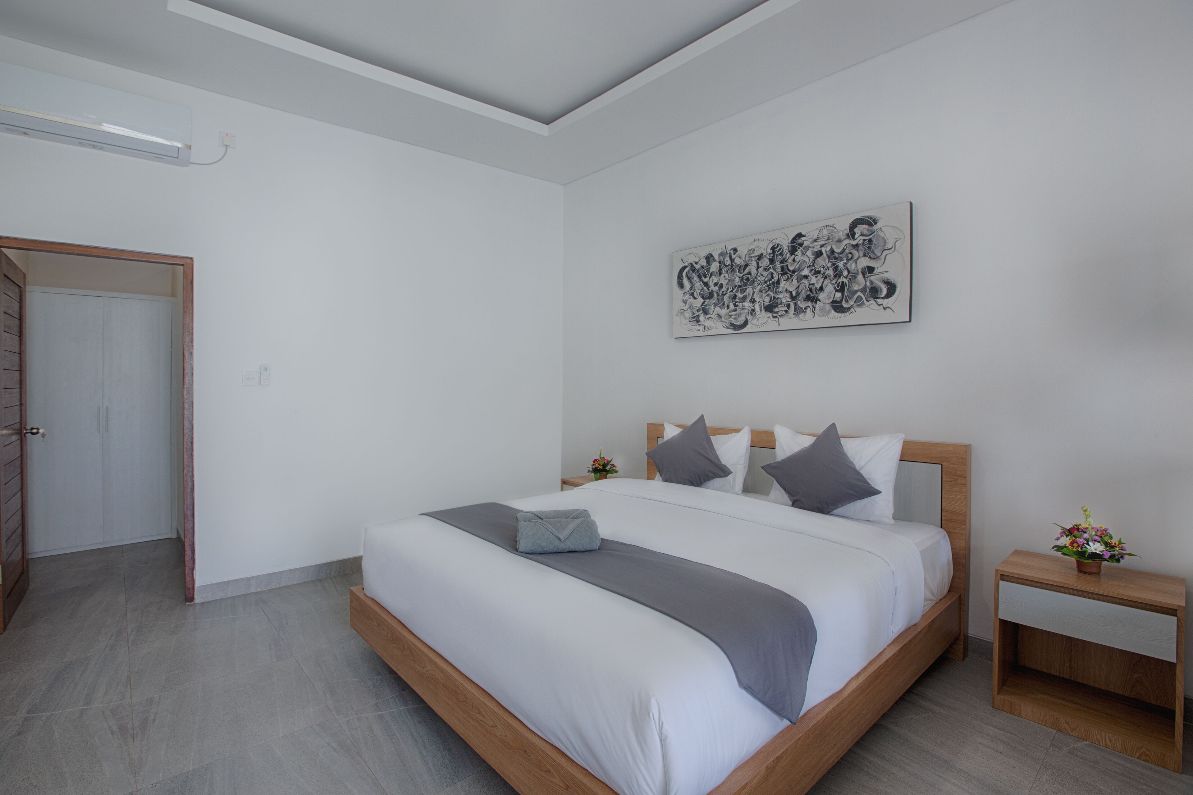 A modern bedroom with a wooden bed frame, white bedding, a grey throw, and a wall-mounted artwork.