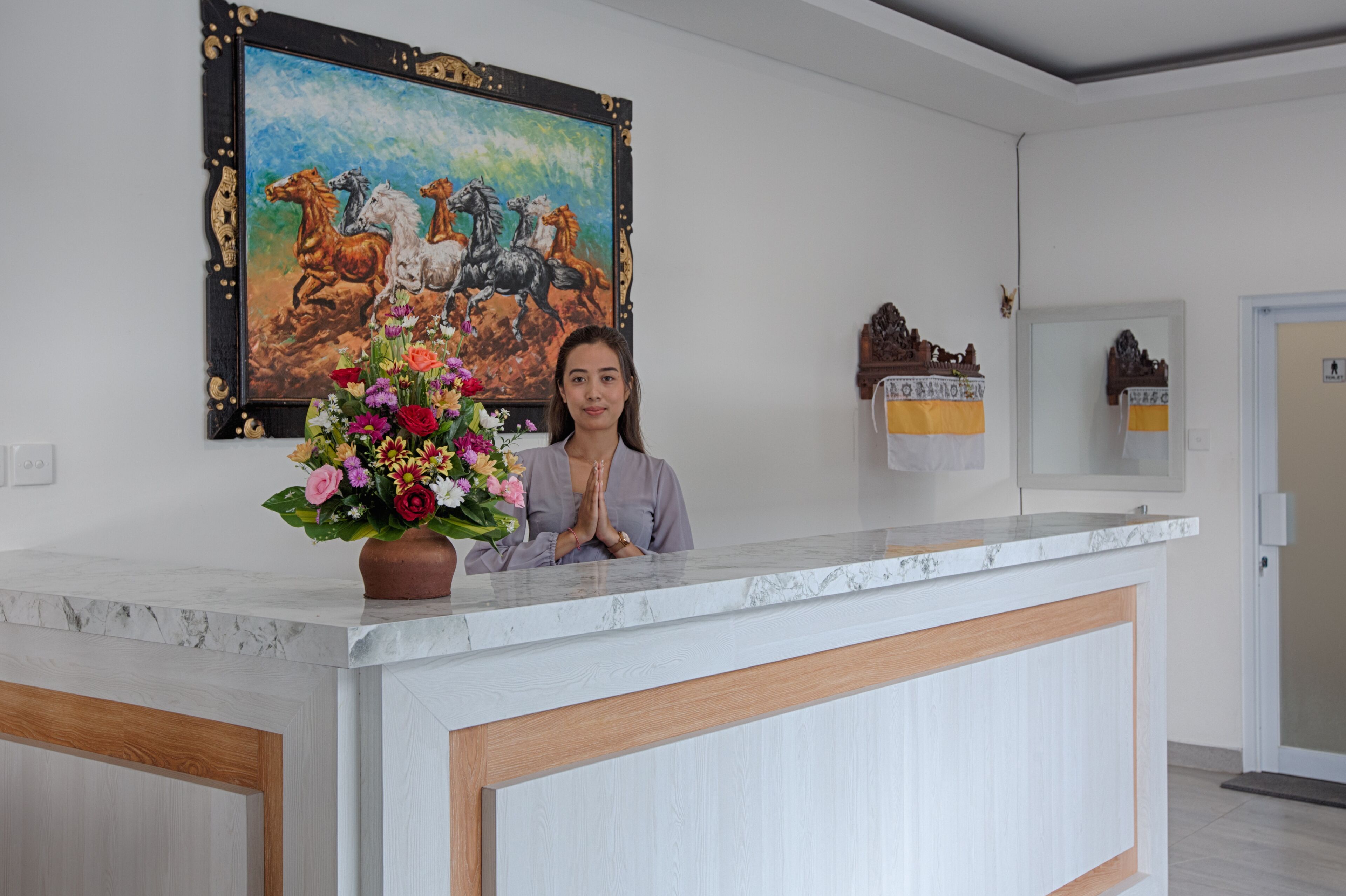 A reception desk with a marble top, a floral arrangement, and a painting of horses on the wall.