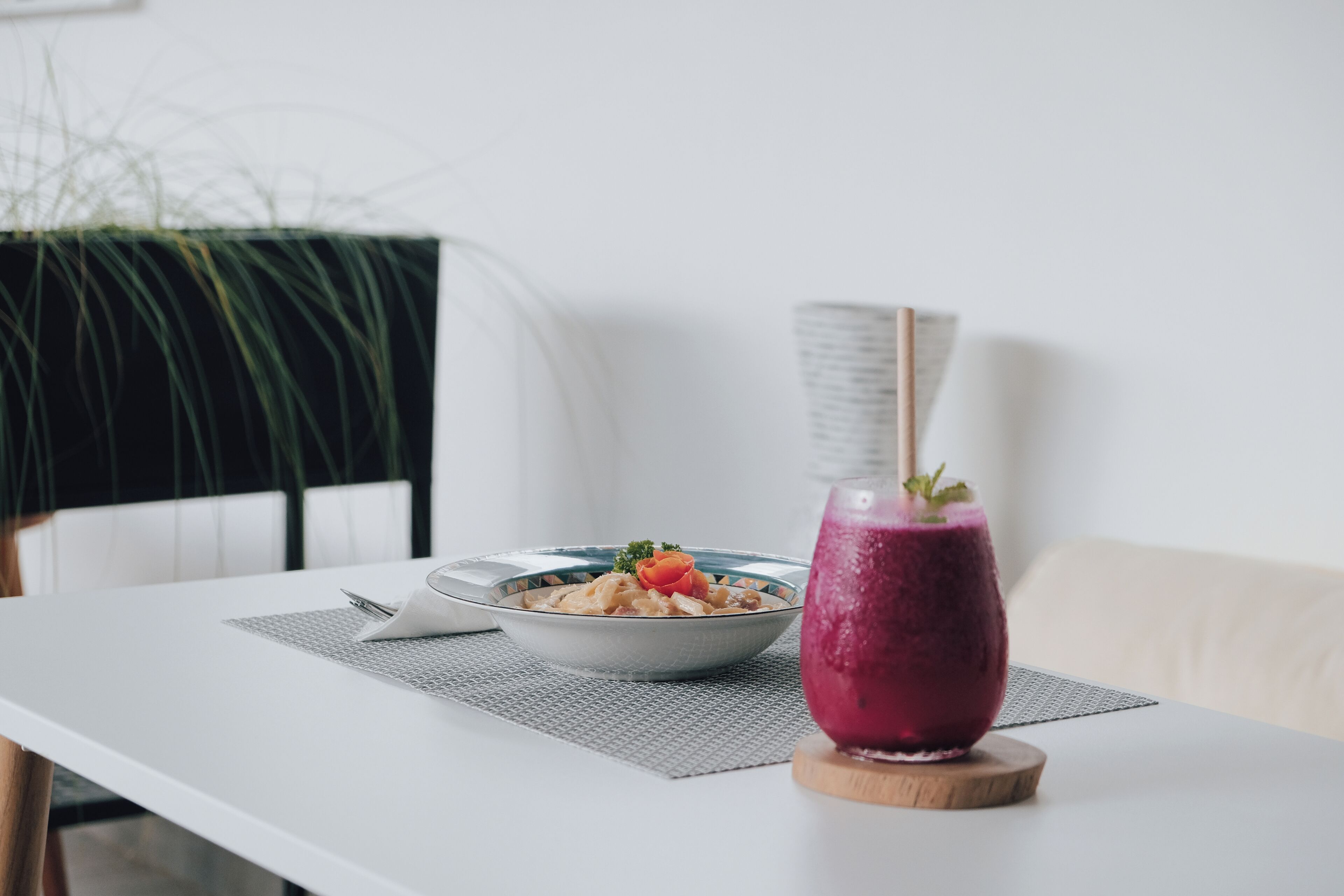 A dining table with a bowl of food and a purple drink on a coaster.