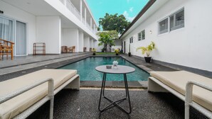 Un espace piscine avec des chaises longues et une table, entouré de murs blancs et surplombé par un ciel dégagé.
