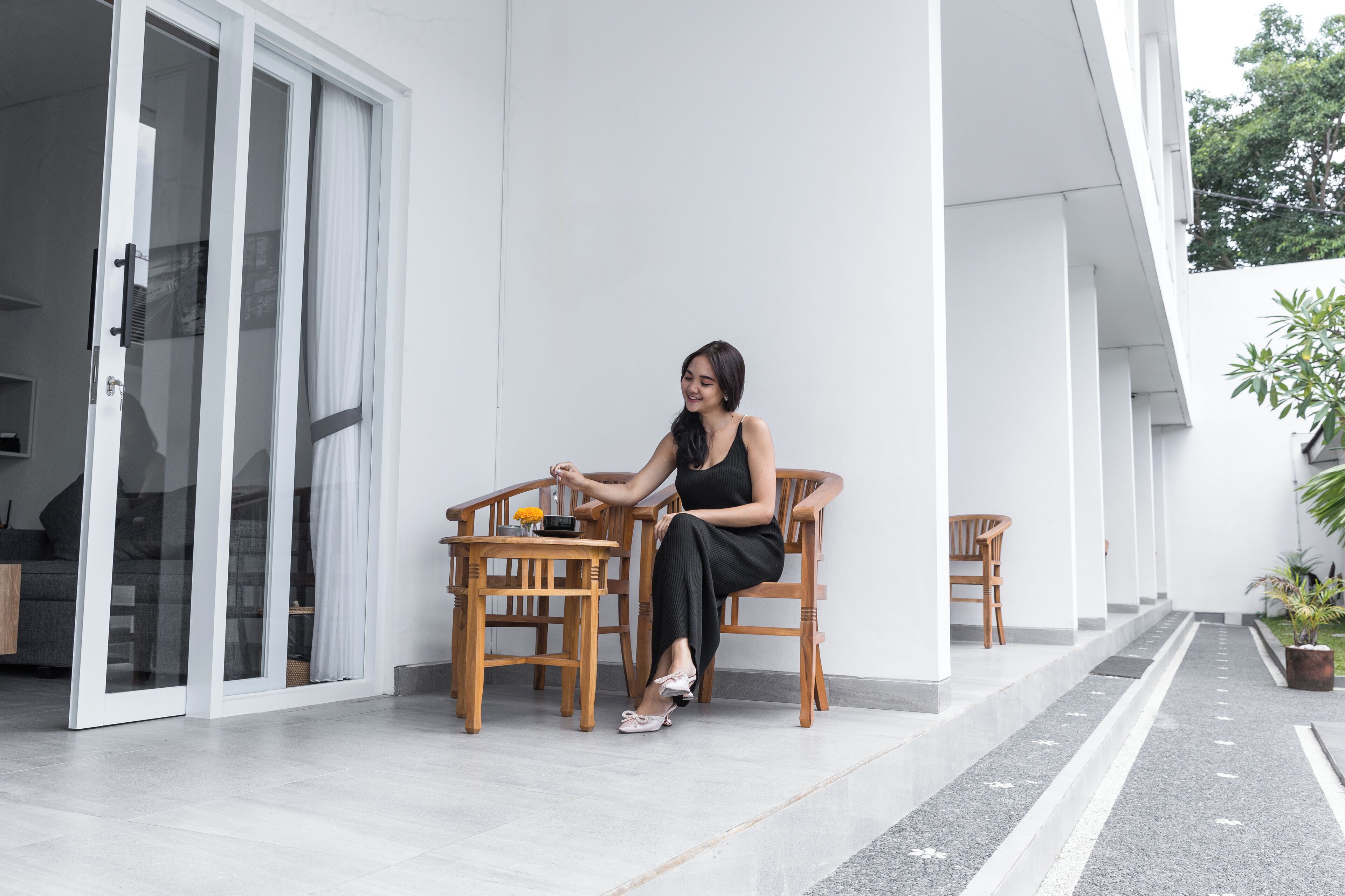 A woman sitting at a table on a balcony with a view of a white building and a garden.