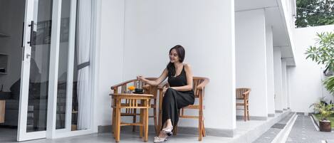 A woman sitting at a table on a balcony with a view of a white building and a garden.
