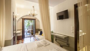 A hotel room with a bed, a TV mounted on the wall, a small table with a chair, and a balcony with a view of the outside. - Superior double room (Neos Marmaras)