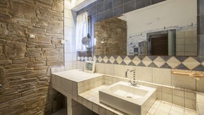A bathroom with a stone wall, a tiled backsplash, a sink, and a mirror.