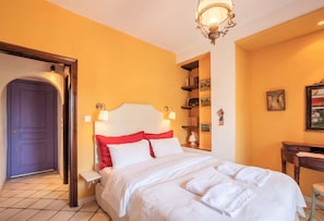 Ein Hotelzimmer mit Bett, Nachttisch, Lampe, Bücherregal und einer Tür.