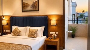 A modern hotel room with a large bed, bedside lamps, a ceiling fan, and a view of the cityscape through an open door. - Hotel Cresent Near Assi Ghat (Varanasi)