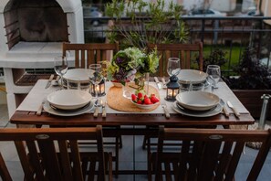 Une table à manger dressée pour quatre personnes, avec des assiettes, des couverts, des verres et un centre de table composé de fraises et de fleurs.