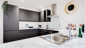 A modern kitchen with dark cabinets, a stainless steel sink, a microwave, and a unique wall clock.