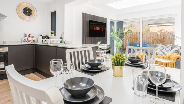 A modern kitchen with a dining area set for a meal, featuring a TV mounted on the wall and a large window.