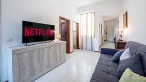 A modern living room with a flat-screen TV displaying "NETFLIX" on the wall, a grey sofa, and a wooden cabinet.
