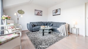 Uma sala de estar moderna com um sofá cinzento, uma mesa de centro redonda, uma poltrona de vime branca e um tapete preto e branco.