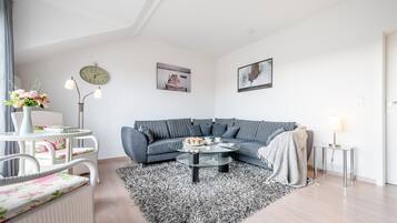 A modern living room with a grey sofa, a round coffee table, a white wicker chair, and a black and white rug.