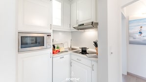 Uma cozinha moderna com armários brancos, micro-ondas embutido, fogão e pia.