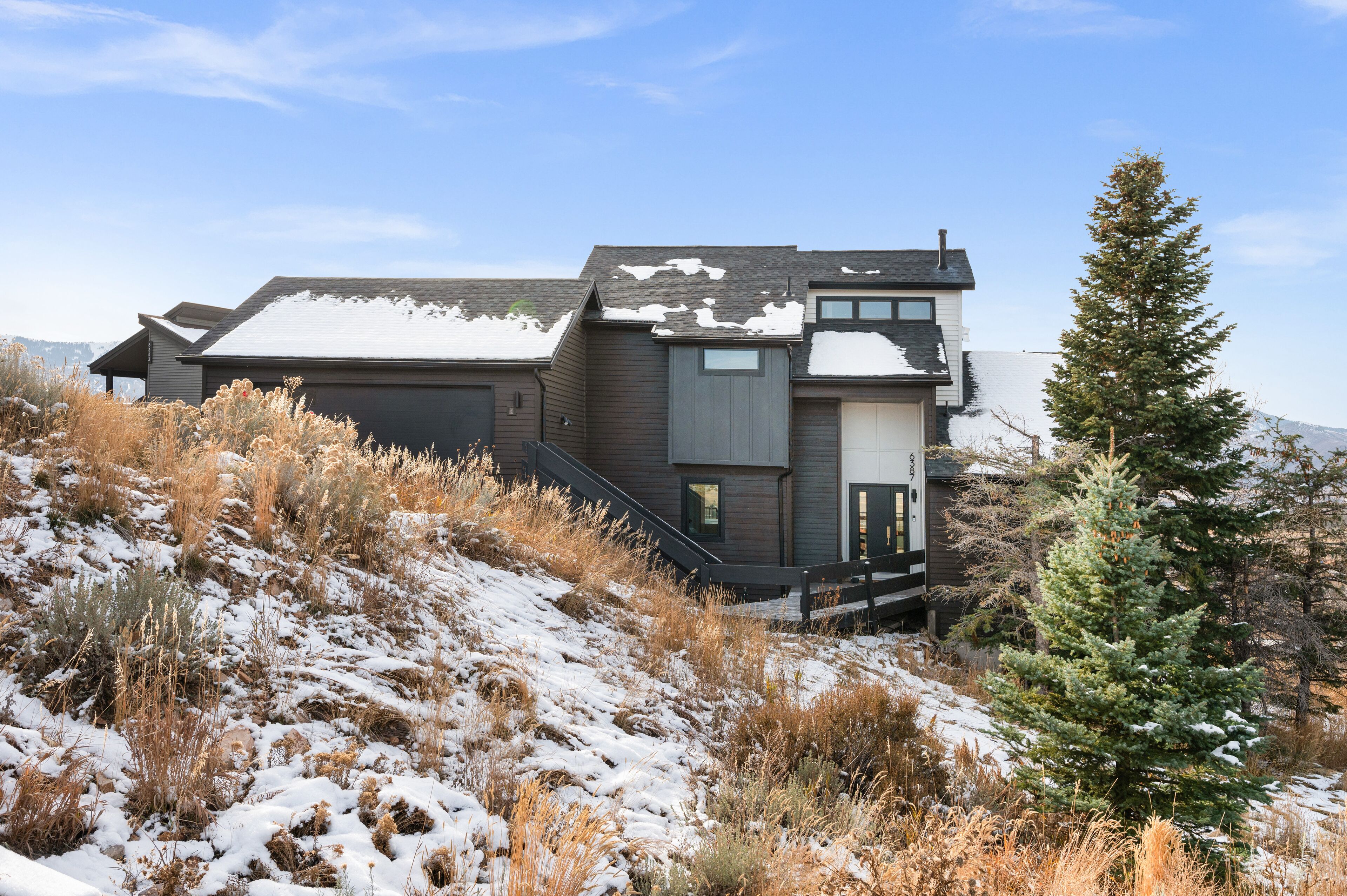 A modern house with a large garage, a covered driveway, and a snow-covered landscape.