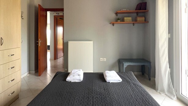 Een slaapkamer met een bed, nachtkastje, kledingkast, radiator en een plank met boeken.