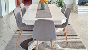 Un espace repas moderne avec une table rectangulaire, des chaises recouvertes d’un tissu gris, un vase central orné de fleurs et un luminaire suspendu.