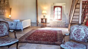 A cozy living room with a large red rug, two upholstered chairs, a glass coffee table, and a wooden staircase.