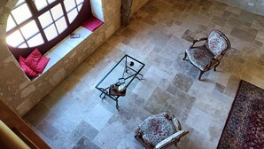 A high-ceiling room with a large arched window, a stone wall, and a tiled floor. There are two upholstered chairs and a small table with a tray.