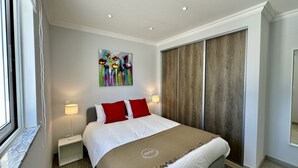 Une chambre d’hôtel avec un lit, deux lampes de chevet, un tableau au mur et une fenêtre avec des stores.