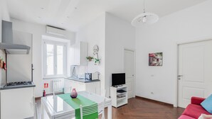 Et moderne køkken med hvide skabe, et spisebord med stole, et fjernsyn på et stativ og en rød sofa i en opholdsstue.