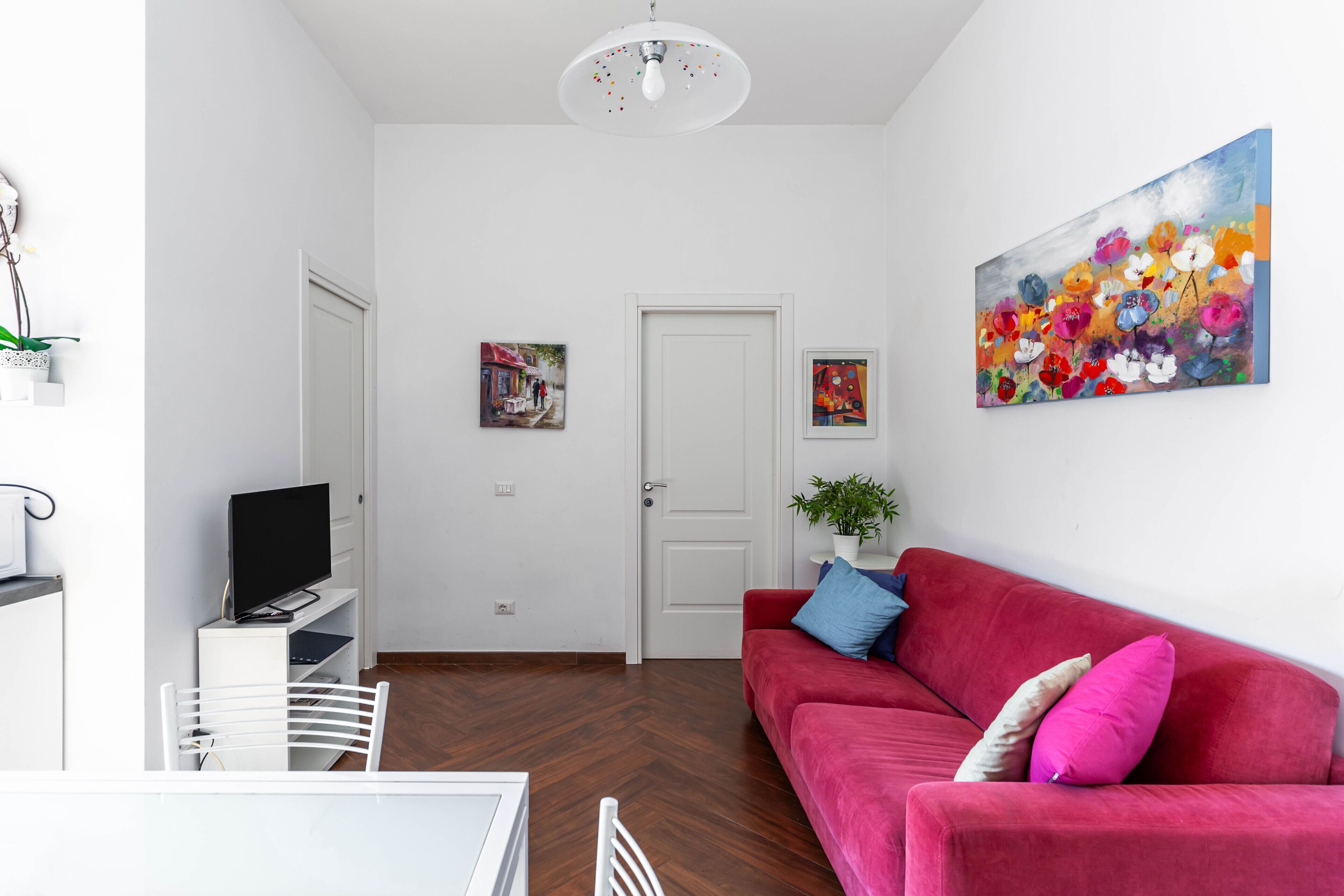 Un salon moderne avec un canapé rouge, des murs blancs et un tableau.