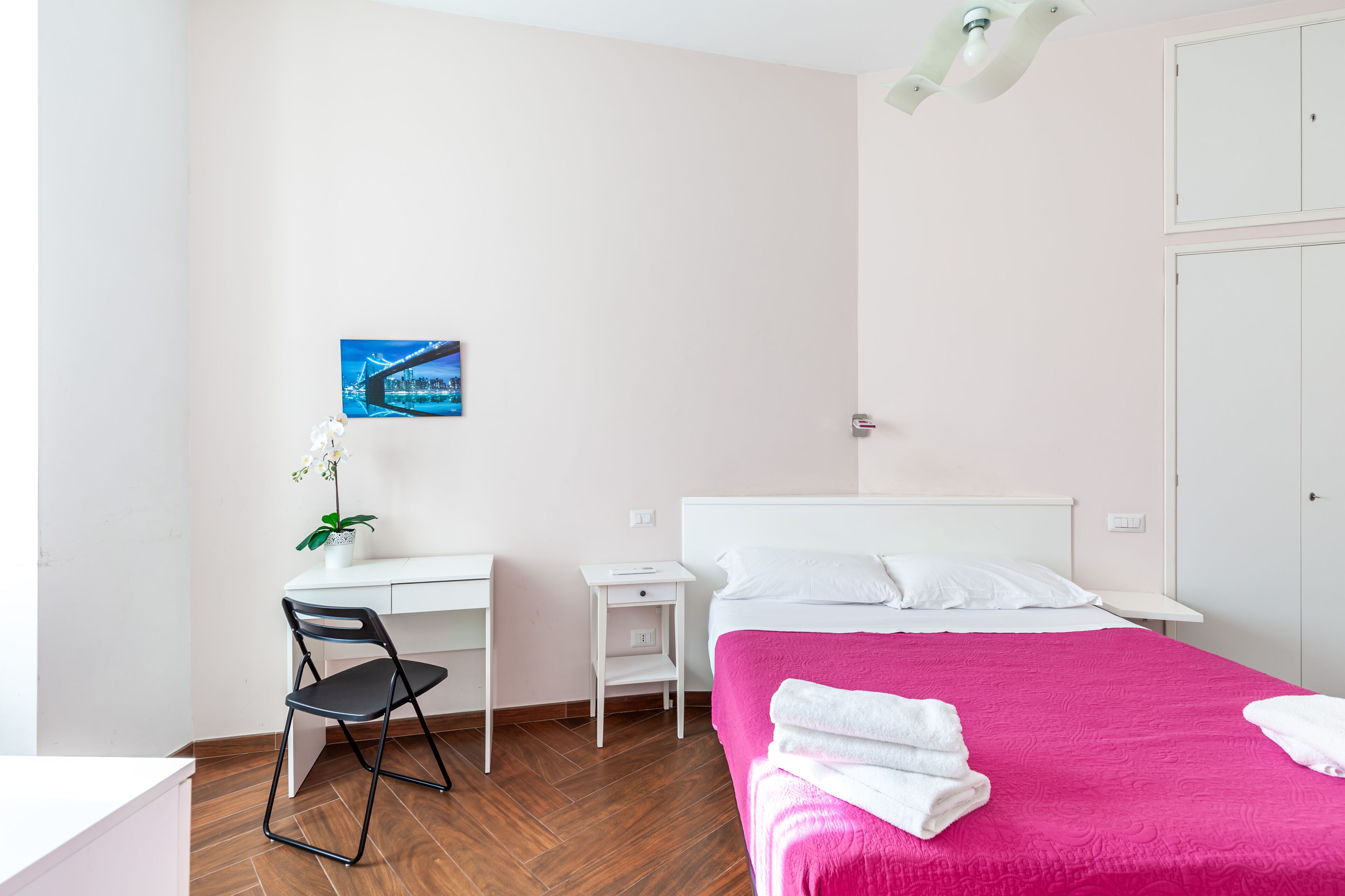 A bedroom with a bed, a desk, a chair, and a nightstand.