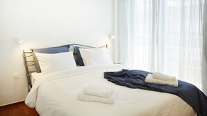 A neatly made bed with white and blue bedding, a dark blue blanket, and two folded white towels. - Luxury Apartment with Exceptional View (Papagou-Holargos)