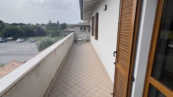 A balcony with tiled flooring, a chair, and a view of a parking lot and distant buildings.