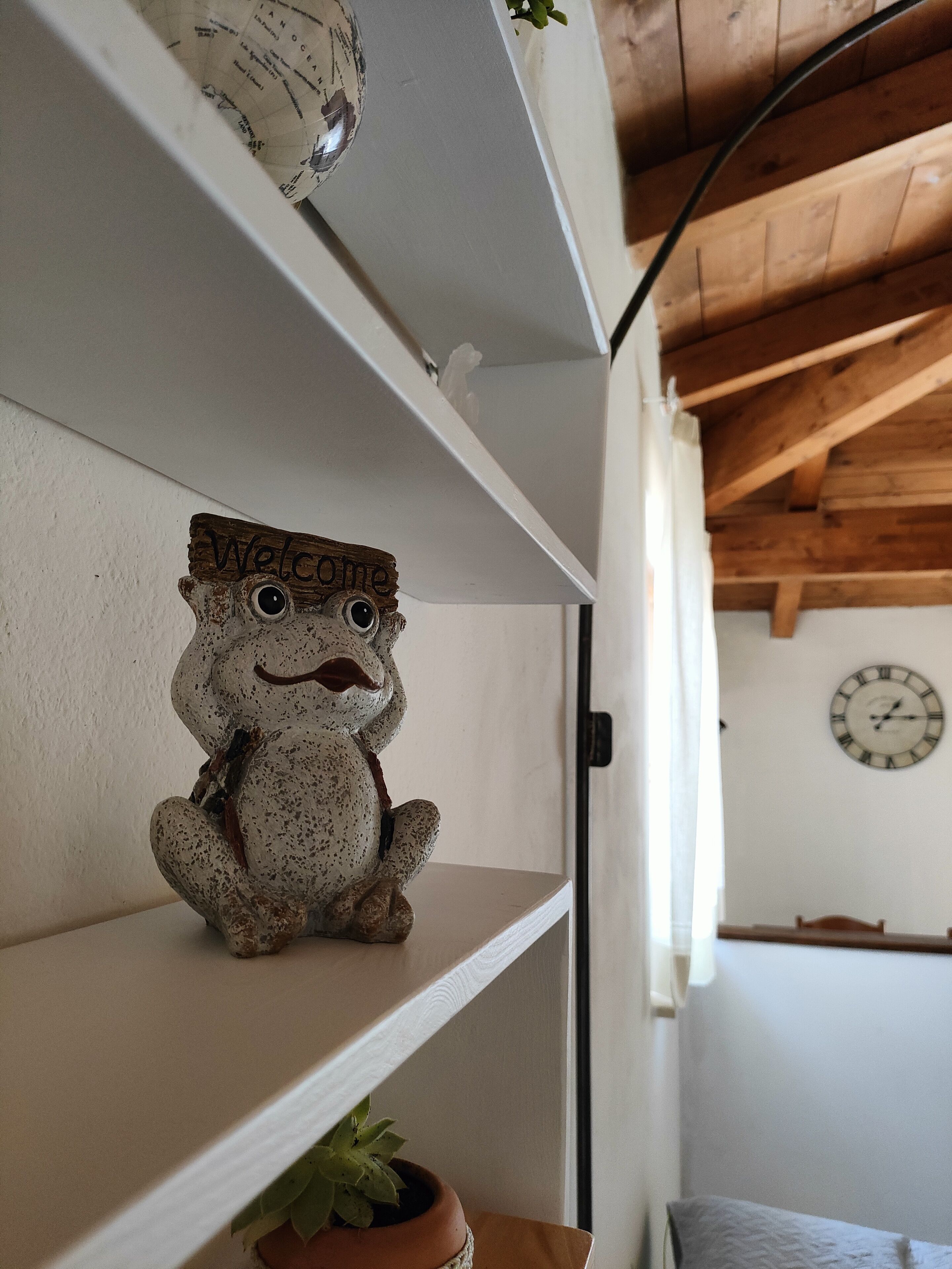 A rustic wooden shelf with a welcome sign, a small clock, and a potted plant.
