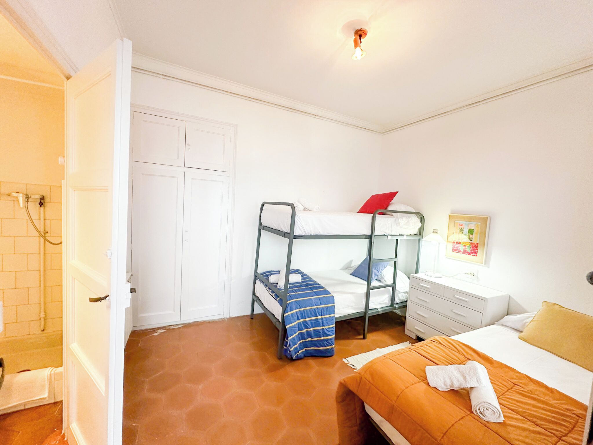 Una habitación con una cama litera, una cama individual, una mesita de noche y un armario pequeño.