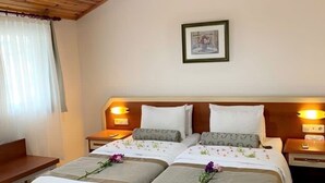 A hotel room with a wooden ceiling, two beds with floral bedding, bedside lamps, a framed picture on the wall, and a bench by the window.