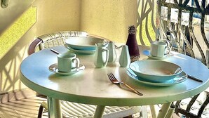 A table set with plates, cups, and a fork on a balcony with a view of the sea and mountains.