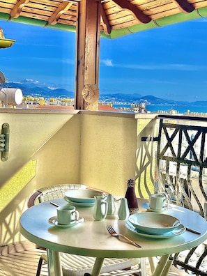 A table set with plates, cups, and a fork on a balcony with a view of the sea and mountains.