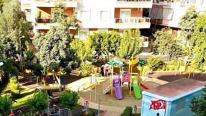 A residential building with multiple balconies, a playground with slides, and a small building with a flag.