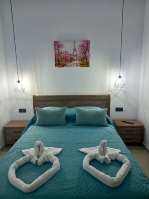 Un dormitorio con una cama, dos mesitas de noche, un cuadro de un parque y dos lámparas colgantes.