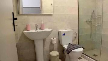 Un baño con lavamanos, inodoro y ducha con mampara de vidrio.