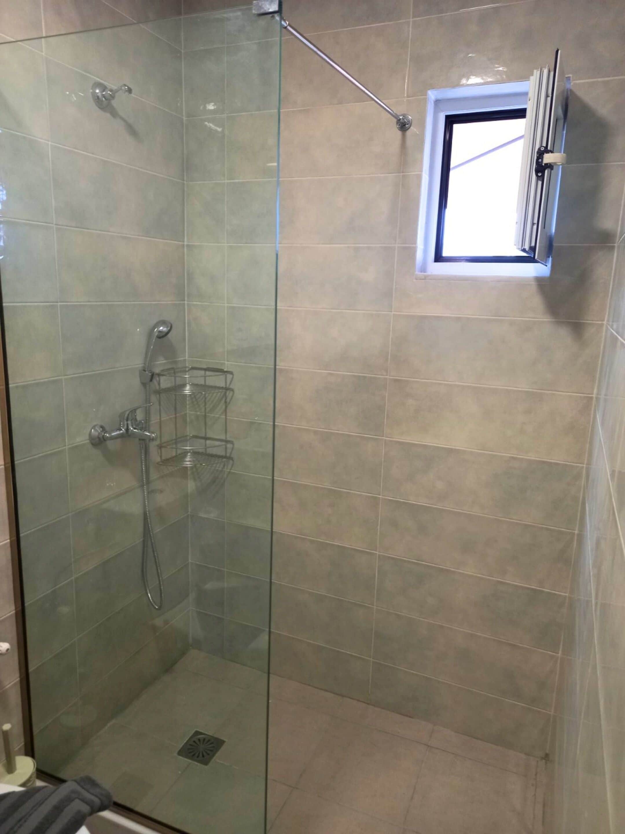 A glass-enclosed shower with a handheld showerhead and a handheld shower attachment.