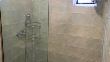 A glass-enclosed shower with a handheld showerhead and a handheld shower attachment.