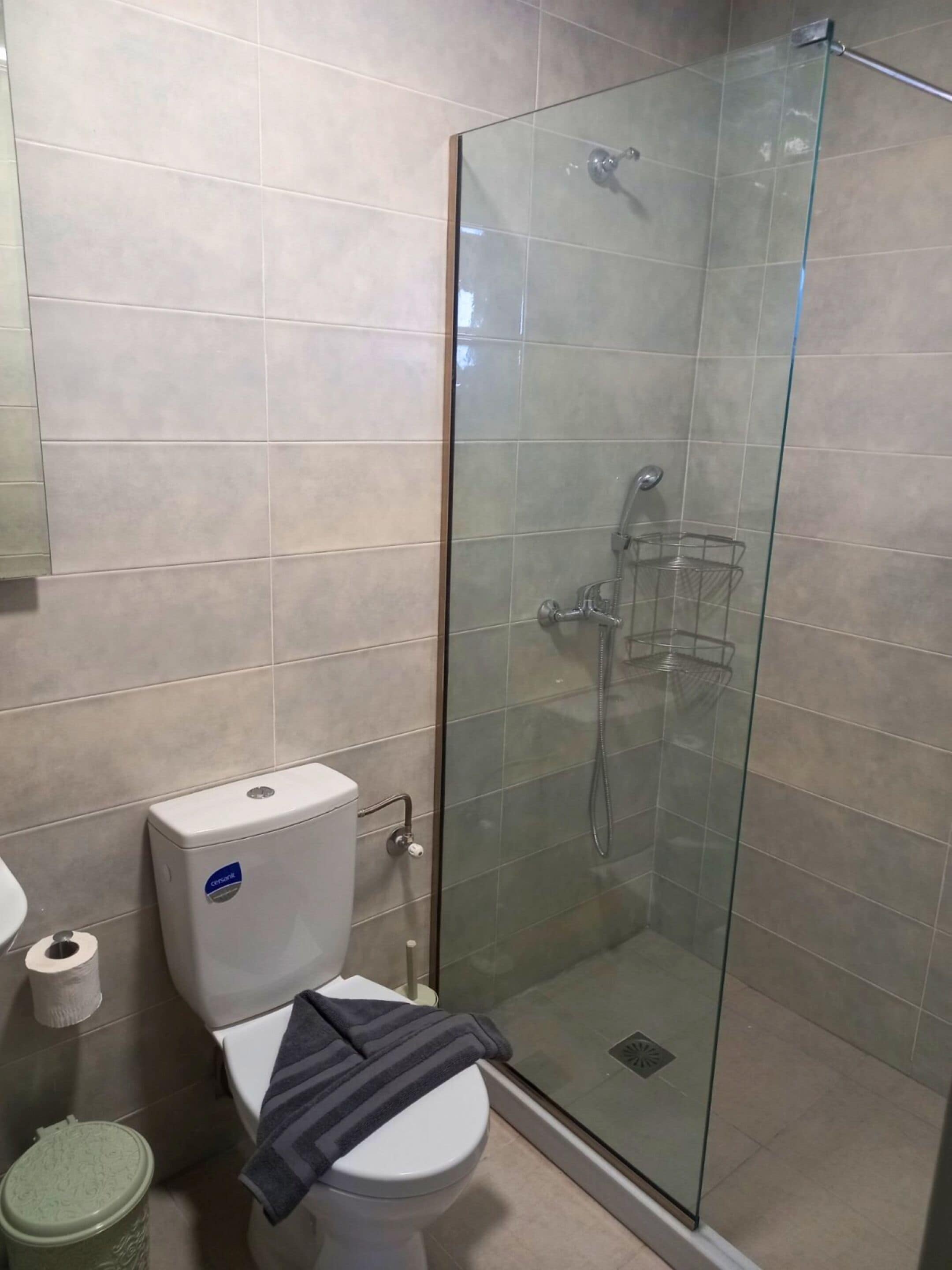 Un baño con inodoro, ducha con cerramiento de vidrio y un cubo de basura.