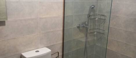 Un baño con inodoro, ducha con cerramiento de vidrio y un cubo de basura.