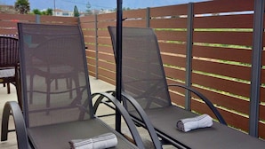 Un patio con dos sillones de descanso bajo una cubierta, una cerca de madera y vista a un campo.