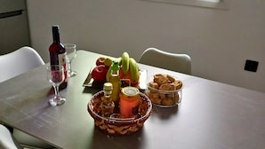 Una mesa de comedor con una botella, vaso, frutas y una cesta de pan.