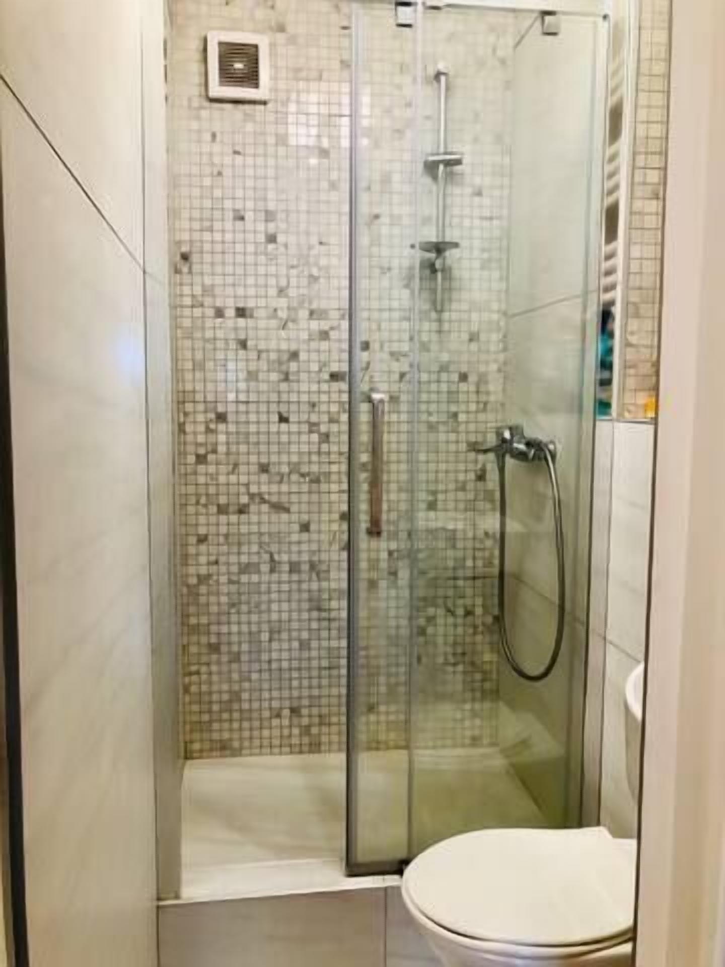 A glass-enclosed shower with a handheld showerhead and a wall-mounted faucet.