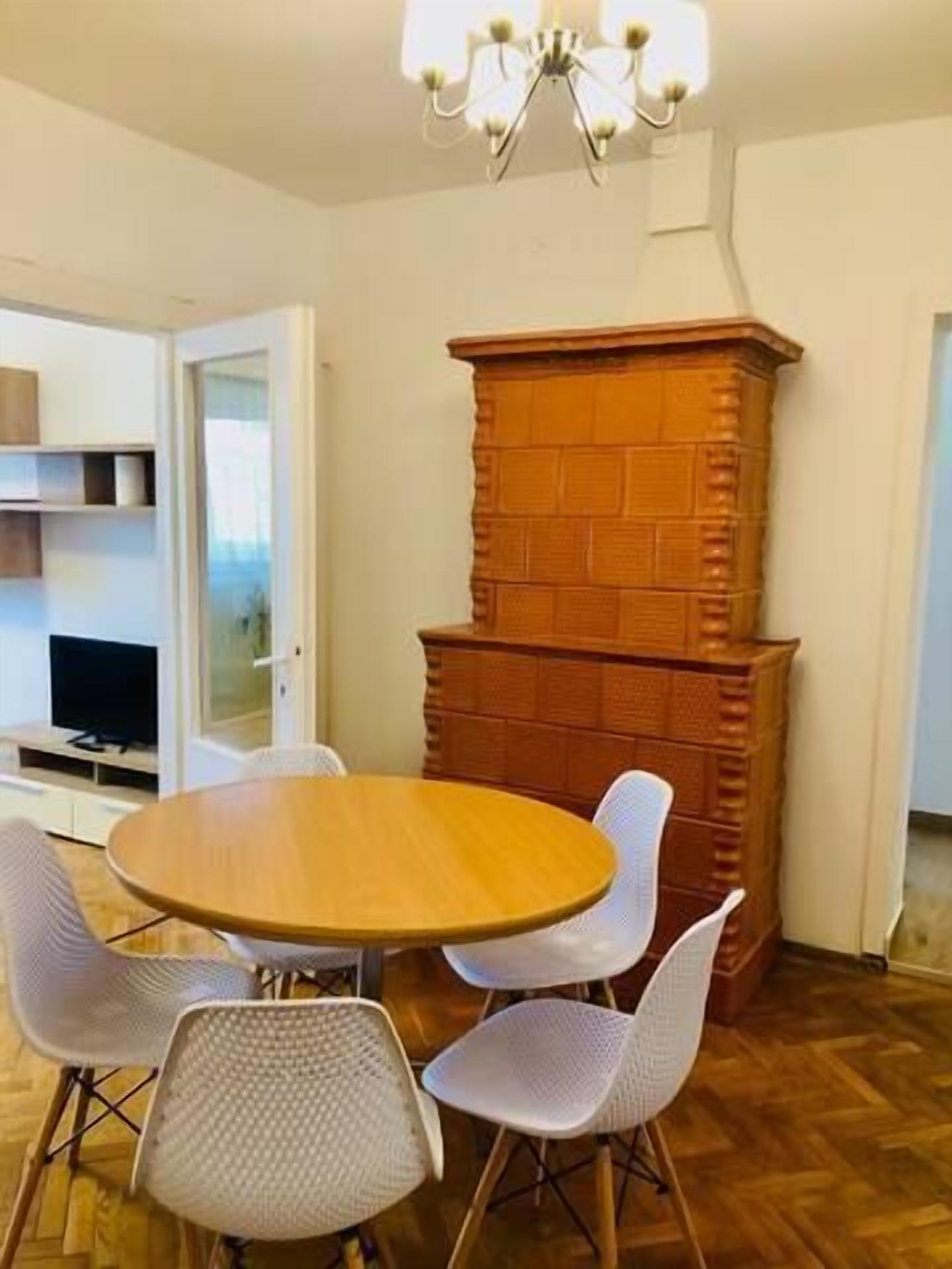 A dining area with a round wooden table and four white chairs. A brick fireplace is in the background.