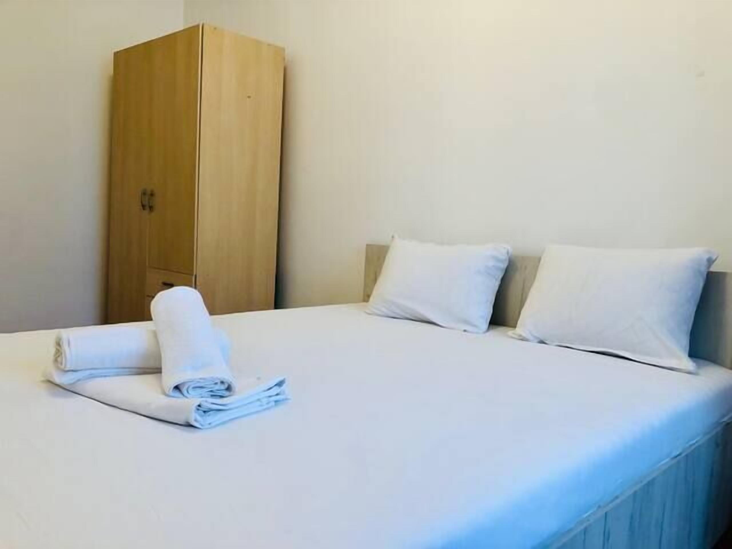 Habitación de hotel sencilla y limpia, con cama, dos almohadas, armario de madera y toallas dobladas con cuidado.