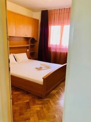 Une chambre avec un lit en bois, une armoire intégrée en bois et une fenêtre avec des rideaux.