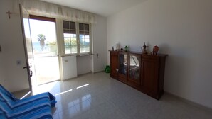 A room with a large sliding glass door leading to a balcony, a wooden cabinet with glass doors, and a striped sofa. - Il Cappero, sul Mare (Porto Badisco, Otranto)