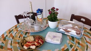A table with a patterned tablecloth, a bottle of champagne, a potted plant, a tray with glasses and condiments, a plate with cheese and olives, a container with bread, and a decorative box. - Il Cappero, sul Mare (Porto Badisco, Otranto)